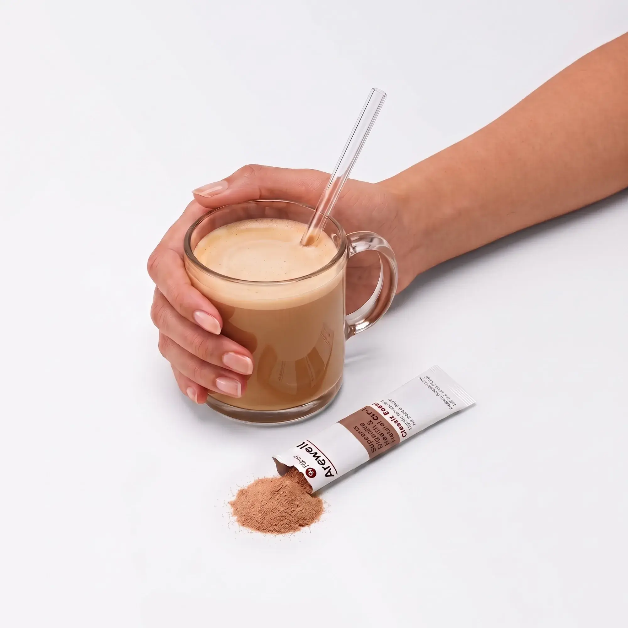 A hand holding a glass mug of Arewell coffee made with milk, with a glass straw. An opened Classic Roast stick pack lies beside it with the coffee powder spilling out.